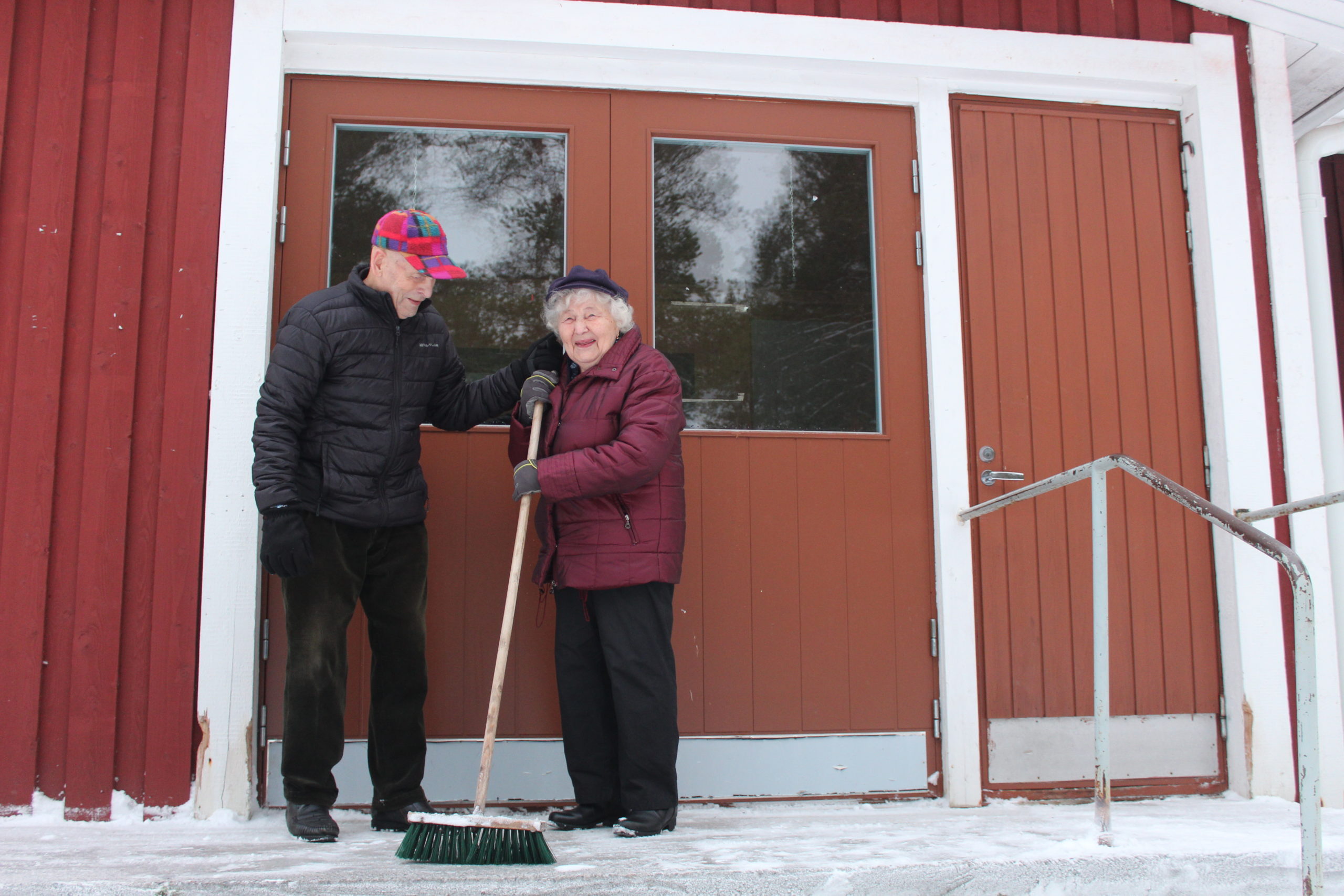 Heikki ja Leena seisovat ja hymyilevät hiihtomajan ulko-oven edessä